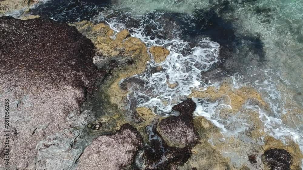 Brandung mit Wasser was auf Steine am Ufer trifft von oben mit Kameraschwenk auf das karibische klare Meerwasser Brandung mit Wasser was auf Steine am Ufer trifft von oben mit Kameraschwenk auf das karibische klare Meerwasser
