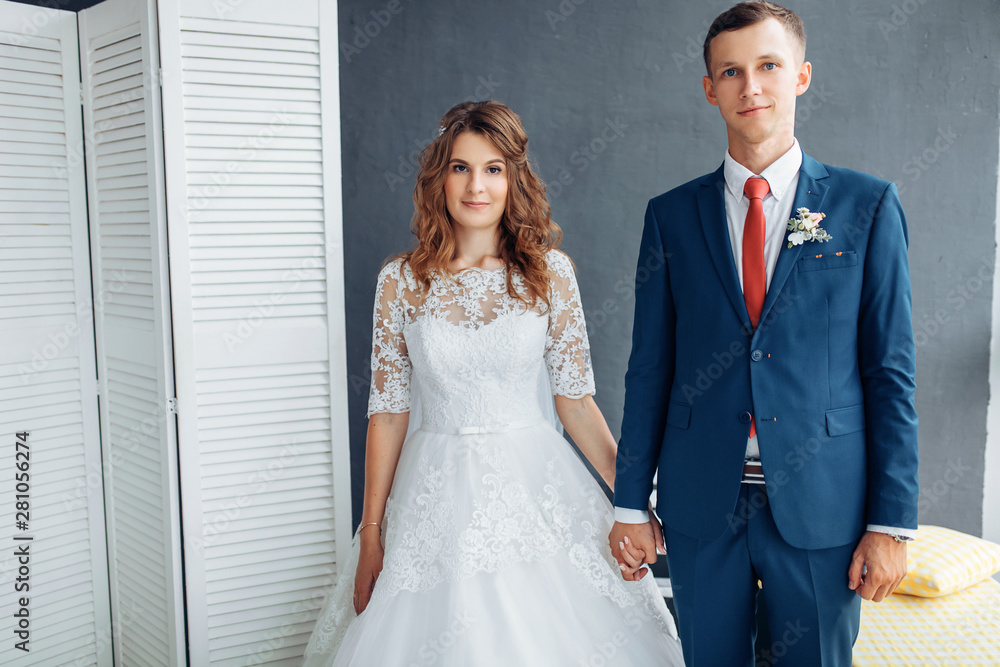 Beautiful bride in white dress and groom in suit, posing in white Studio interior, wedding Beautiful bride in white dress and groom in suit, posing in white Studio interior, wedding