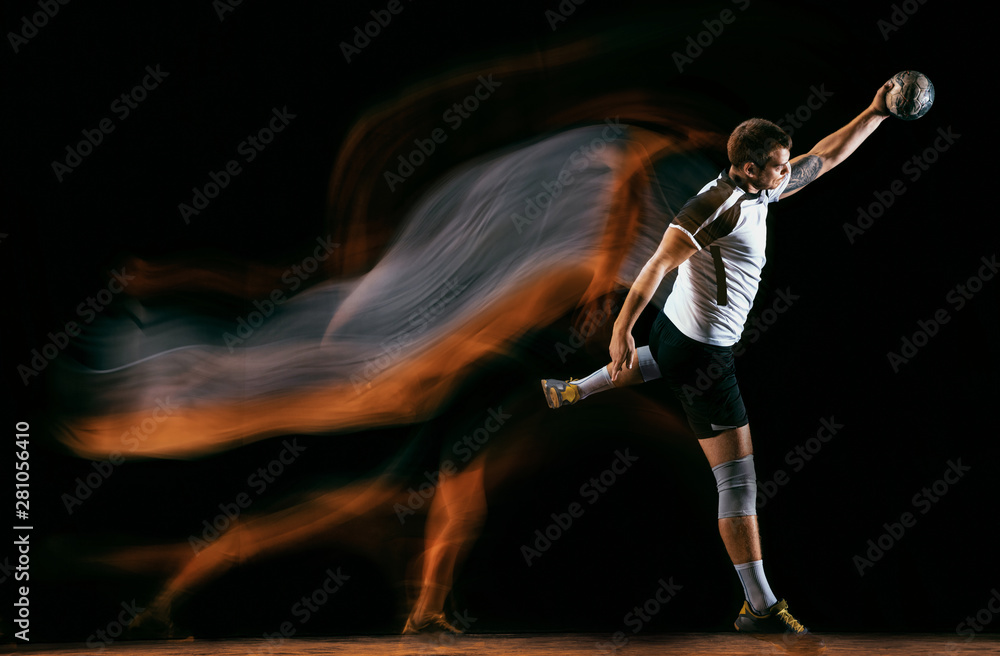 Caucasian young handball player in action and motion in mixed lights over black studio background. Fit male professional sportsman. Concept of sport, movement, energy, dynamic, healthy lifestyle.