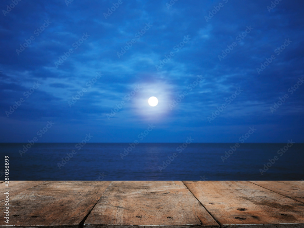 Wooden table top over summer beach at night with full moon  background.