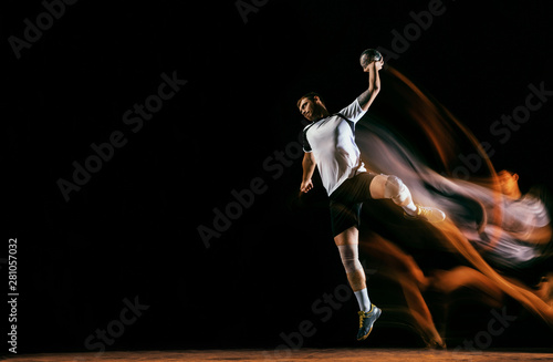 Caucasian young handball player in action and motion in mixed lights over black studio background. Fit male professional sportsman. Concept of sport, movement, energy, dynamic, healthy lifestyle.