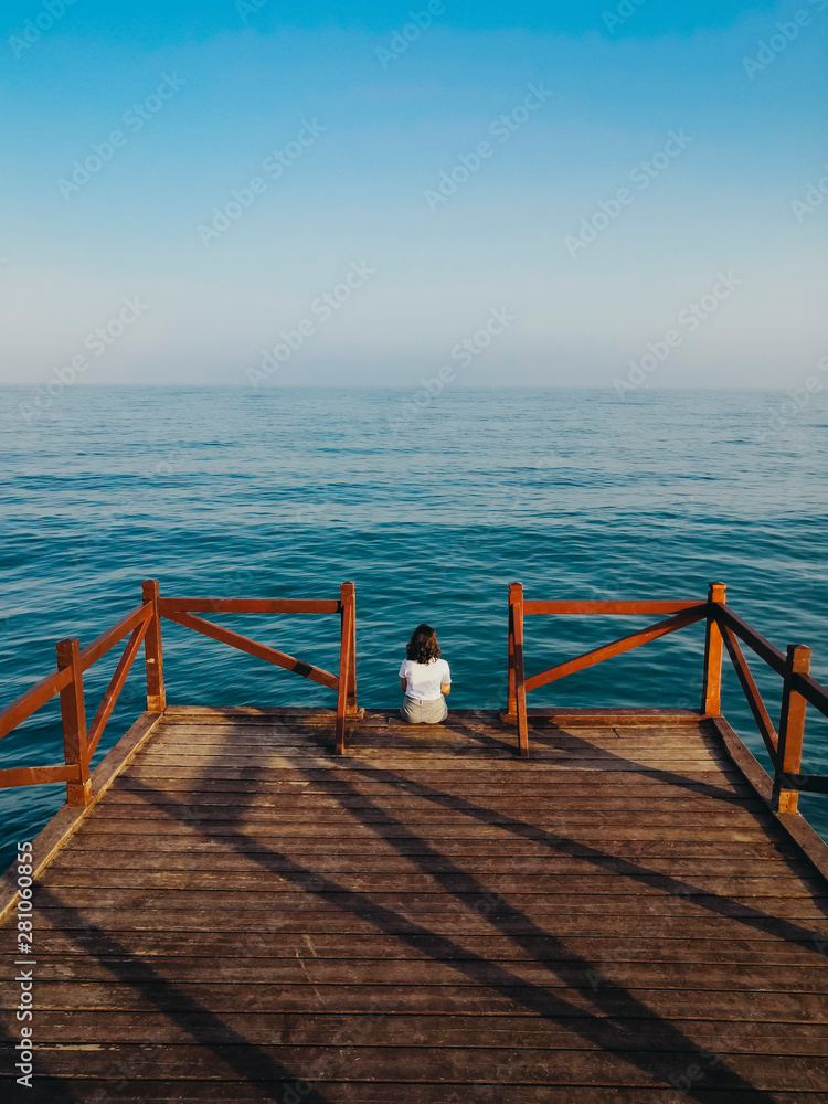 Young girl looking at the horizon on a wooden jetty over the sea Young girl looking at the horizon on a wooden jetty over the sea