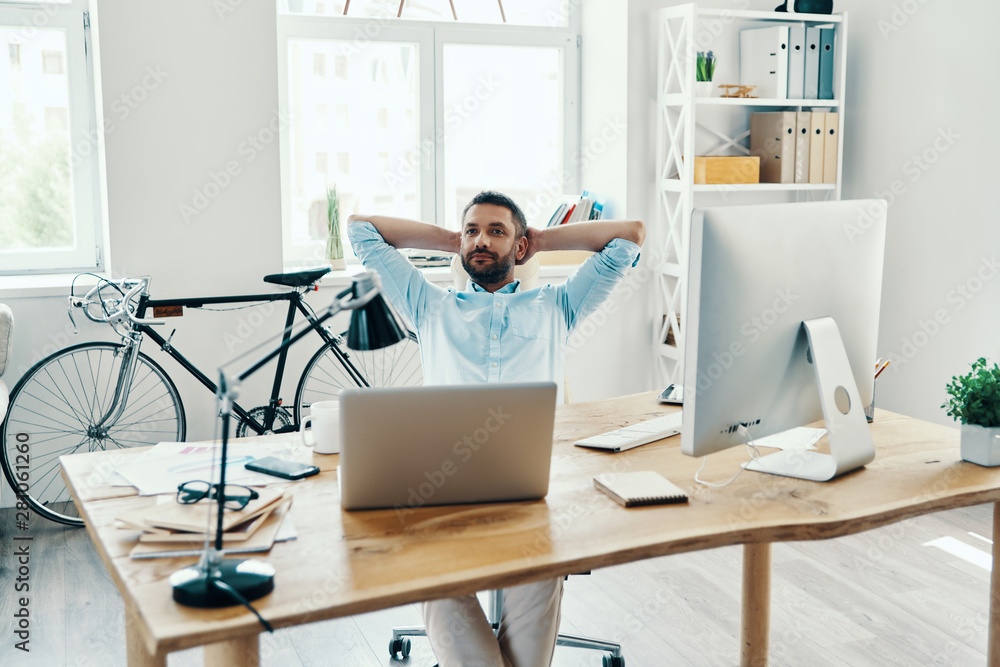 Relaxed middle age man in smart casual wear keeping hands behind head while sitting in the office Relaxed middle age man in smart casual wear keeping hands behind head while sitting in the office