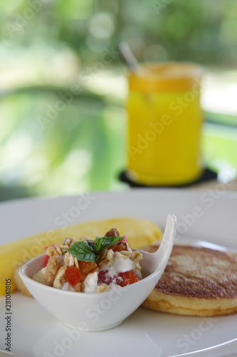 Breakfast served on the table, fruit salad with muesli, American pancake, omelet and a glass of fresh orange juice