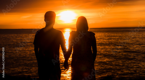 Young couple - Asian man and his pregnant wife watching the sun set over the sea