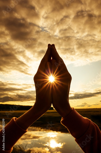 Tin namaste close-up, the sun shines between the fingers with stunning rays. Silhouette against the setting sun, sky and river. Concept of amateur yoga, healthy lifestyle, meditation practice.  photo