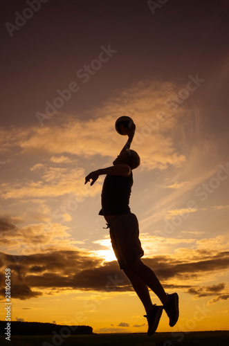 Silhouette of a man with a short haircut in a T-shirt and shorts with a ball. The concept of games with a ball in the fresh air, volleyball. Photo in warm sunset colors. Place for text.  © Ольга Холявина