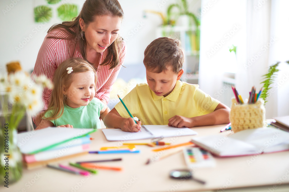 mother daughter and son draws pencil on a sheet of paper sitting at home at the table in a bright room. mother daughter and son draws pencil on a sheet of paper sitting at home at the table in a bright room.