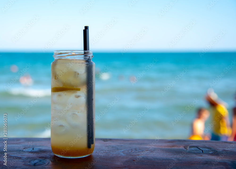 A jar of lemonade, in which float lemon and ice, with two black tubes, on the bar against the sea. A jar of lemonade, in which float lemon and ice, with two black tubes, on the bar against the sea.