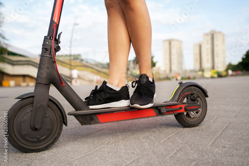 Closeup female legs on electric push scooter , city buildings in background 
