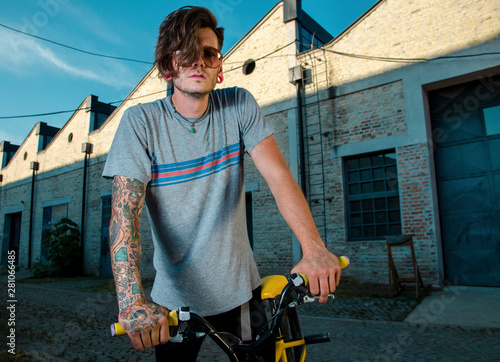 Tattooed guy on BMX bike, outdoors on the streets