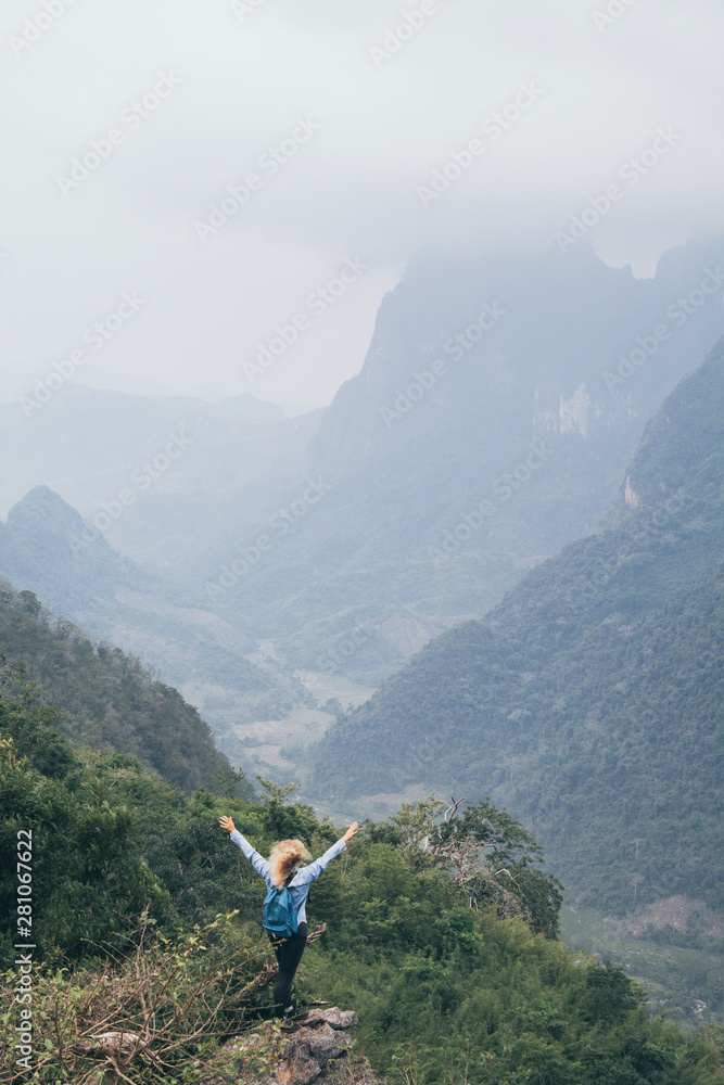Young Caucasian woman standing on the top of the mountain overlooking river valley in Nong Khiaw village, Laos