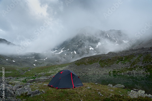tourist tent near the mountain lake in the background of the mountain Dzhalkaush in the mist of low clouds, Teberda, Karachay-Cherkessia, Russia