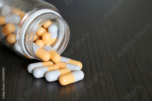 Capsules spilled from the bottle, white-yellow pills on vintage dark wooden table. Concept of pharmacy, antibiotics, vitamins