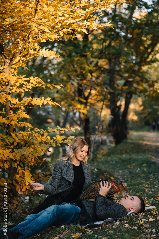 Beautiful young couple resting in autumn park. autumn concept. Loving couple resting with their cat. Beautiful young couple resting in autumn park. autumn concept. Loving couple resting with their cat.
