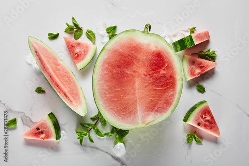 top view of cut delicious exotic red watermelon with seeds on marble surface with ice and mint