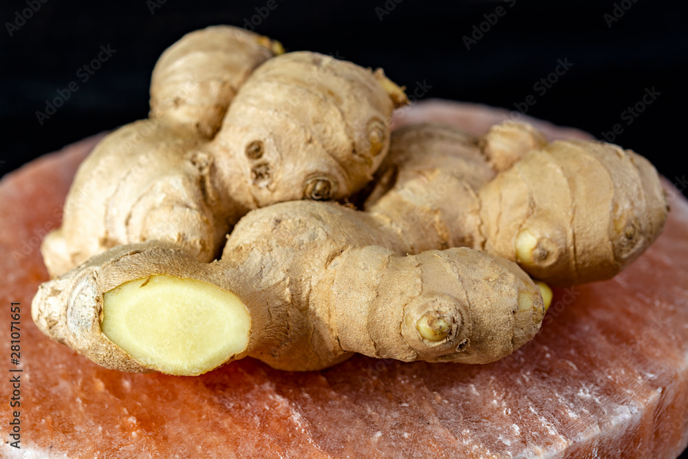 Fototapeta premium Fresh ginger roots on pink salt board close up on black wooden background