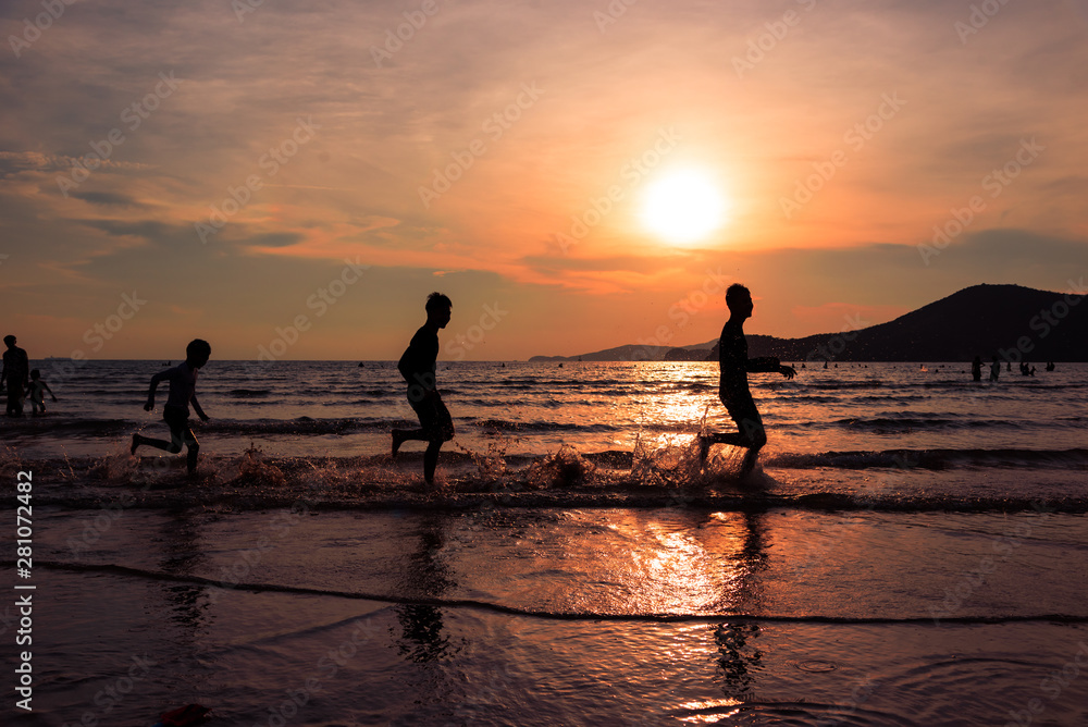 Silhouette young boys running on the sand beach and sunset seascape background.Happy and funny time together concept.