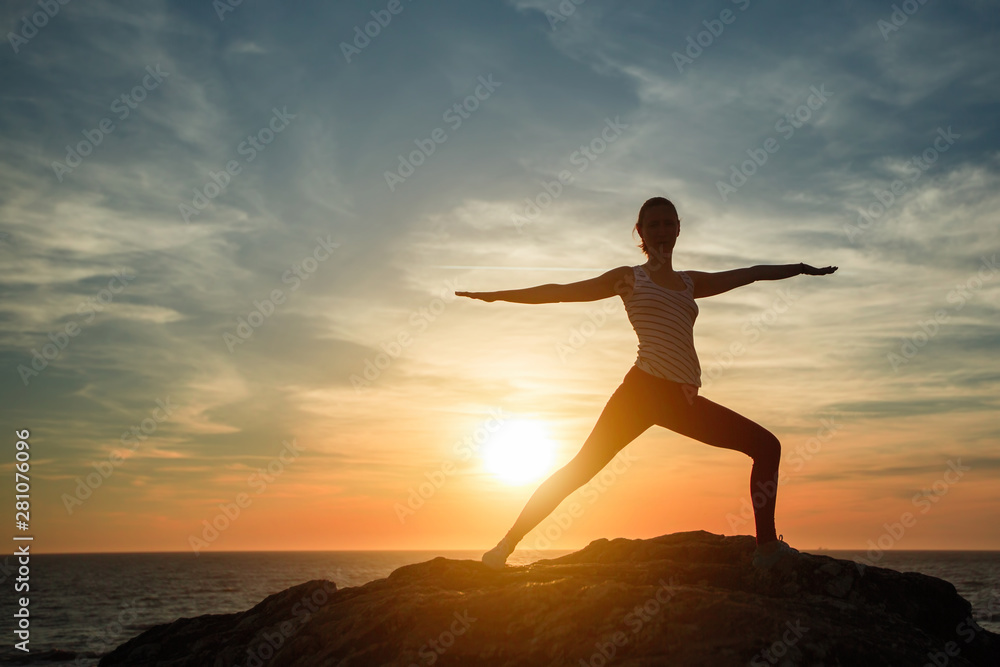 Silhouette of yoga woman doing fitness exercises on ocean beach at sunset.