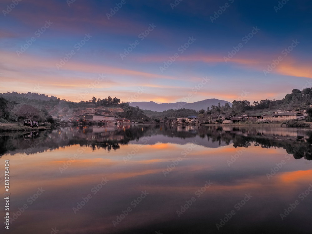 view morning of Ban Rak Thai Village on the bank of reservoir with green hill and red sun light in the sky background, Ban Rak Thai Reservoir, Mae Hong Son, northern of Thailand.