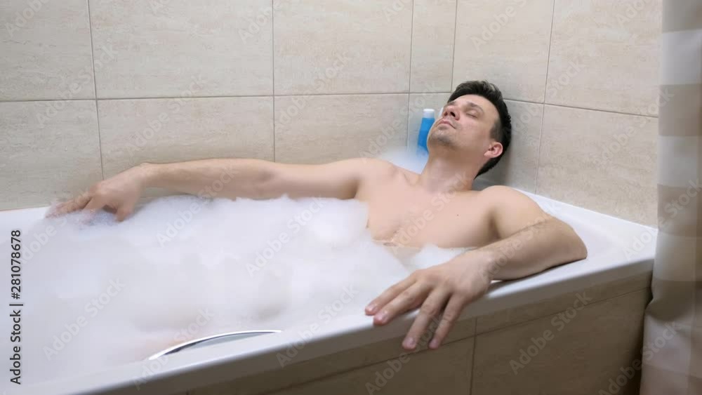 30s man sitting in the bathroom, relaxing and falling asleep in the evening in foam after hard day. 30s man sitting in the bathroom, relaxing and falling asleep in the evening in foam after hard day.