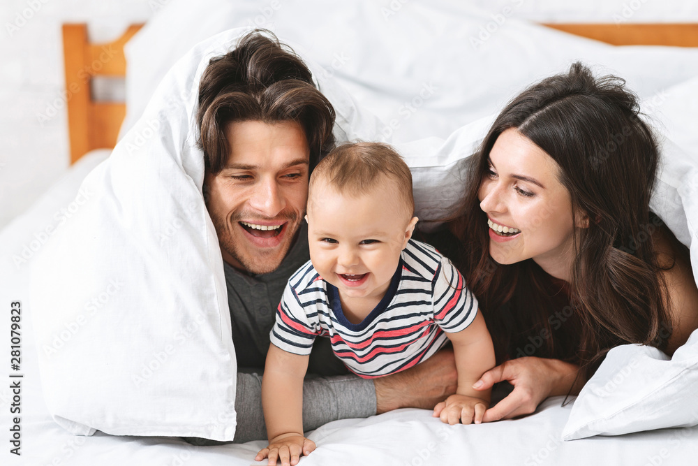 Cheerful parents playing with baby son in bed