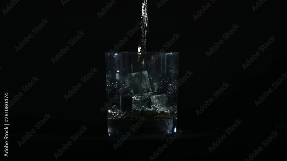 Slow Motion. In front of a black background, whiskey is poured into a glass of whiskey stones. Slow Motion. In front of a black background, whiskey is poured into a glass of whiskey stones.