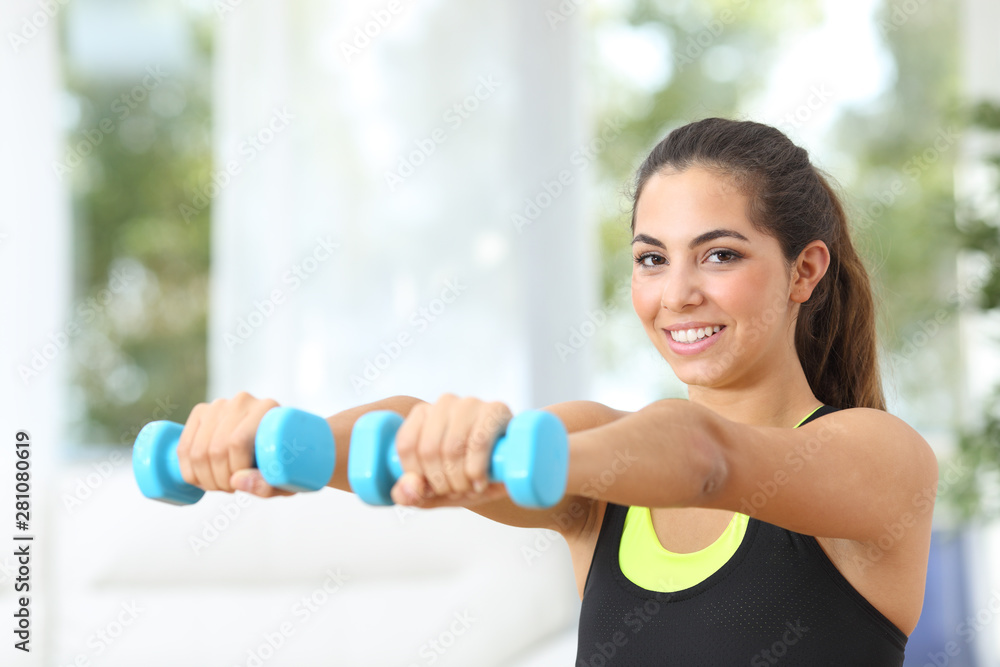 Happy sportswoman lifting weights looking at you
