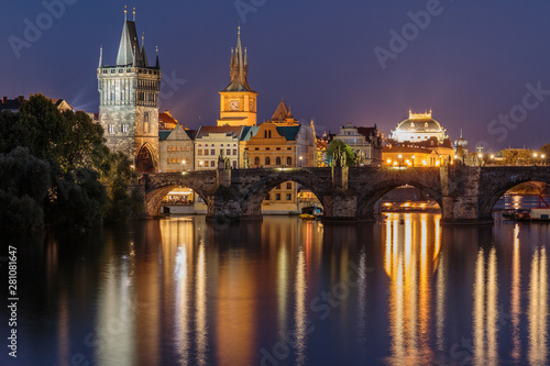 Panoramic view over the river Vltava to Charles Bridge at night in Prague. Old Town tower and historic stone bridge with lighting between the old town and the Lesser Town and reflections on the water.