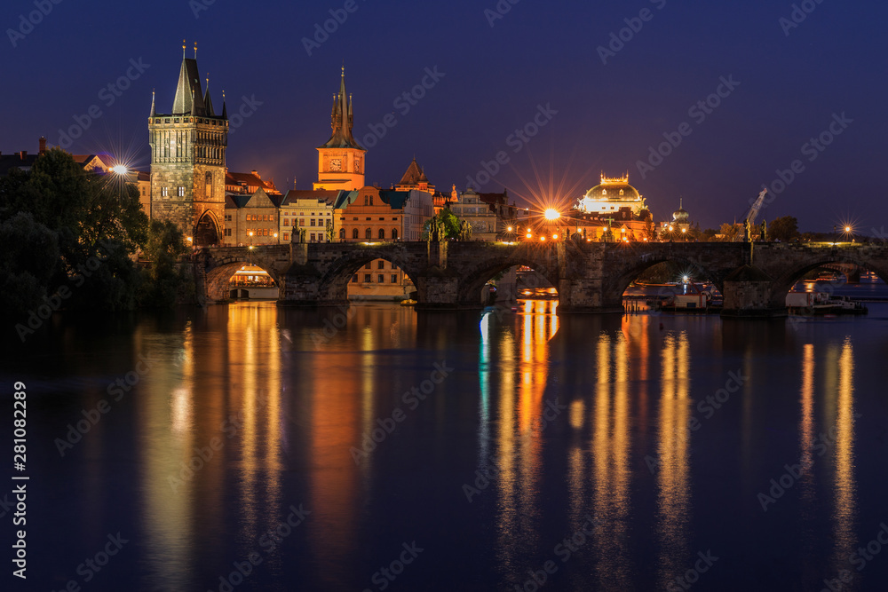 Prague with Charles Bridge at night. Panoramic view over the Vltava. Old Town tower and historic stone bridge with lighting between the old town and the Lesser Town and reflections on the water