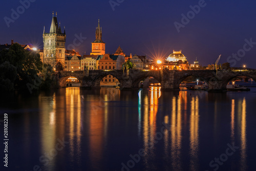 Prague with Charles Bridge at night. Panoramic view over the Vltava. Old Town tower and historic stone bridge with lighting between the old town and the Lesser Town and reflections on the water