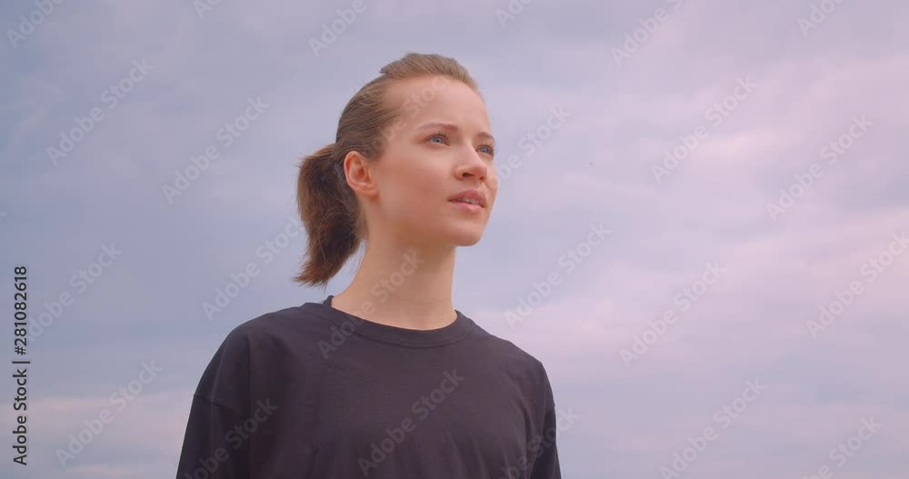 Closeup portrait of young positive sporty female jogger in a black t shirt smiling happily looking forward with pink sky on the background in urban city outdoors Closeup portrait of young positive sporty female jogger in a black t shirt smiling happily looking forward with pink sky on the background in urban city outdoors