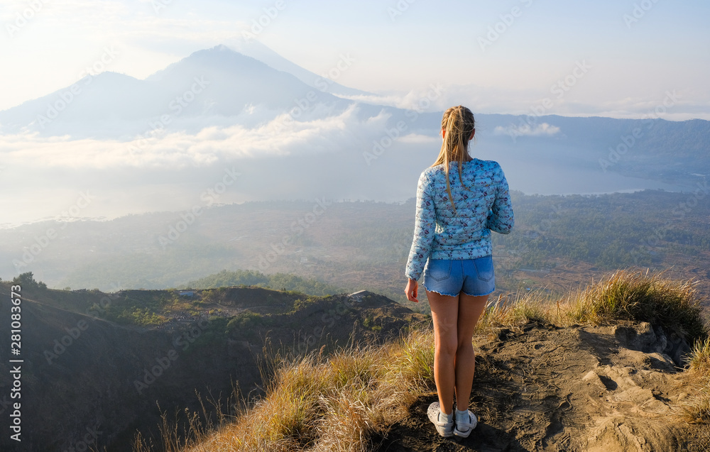 The girl meets the dawn at the top of the volcano Batur, Bali, Indonesia. Dawn on the background of Agung volcano.