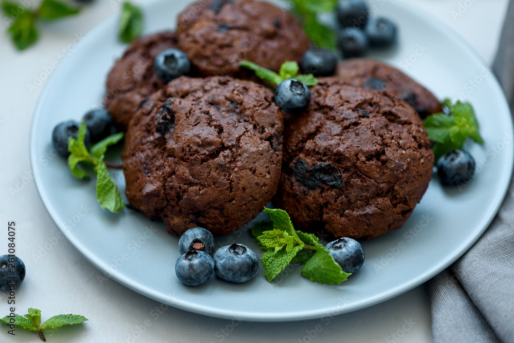 Chocolate cookies with chocolate chips and blueberry on gray wooden background. Summer food. Soft focus. Chocolate cookies with chocolate chips and blueberry on gray wooden background. Summer food. Soft focus.