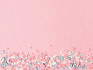 Festive border frame of colorful pastel sprinkles on pink background, copy space top. Sugar sprinkle dots and stars, decoration for cake and bakery. Top view or flat lay