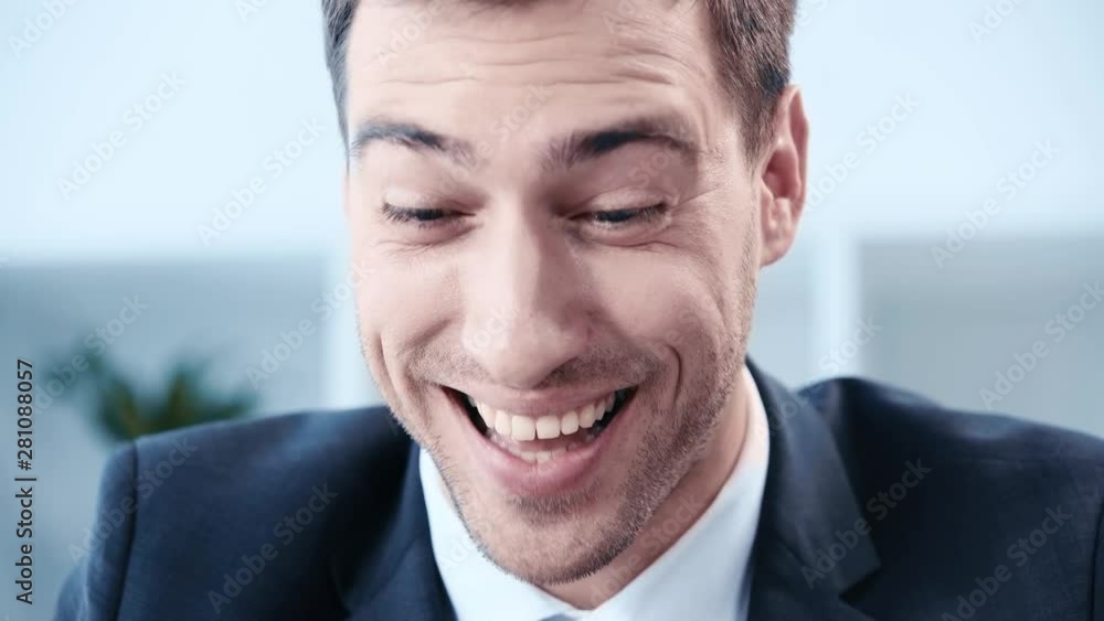 handsome, cheerful businessman laughing while using laptop in office handsome, cheerful businessman laughing while using laptop in office