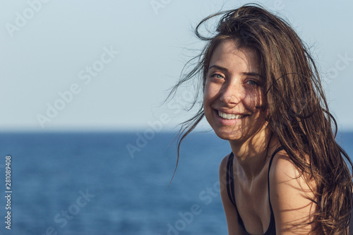 Close-up portrait of cheerful suntanned young woman over sea and blue sky background. Photo of beautiful brunette girl relaxing on the resort under the hot sun. Image of summer and vacation concept.