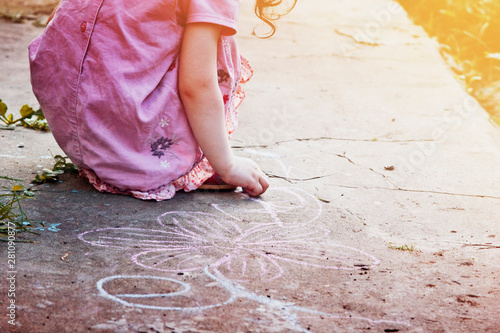 Little girl draws with chalk on asphalt
