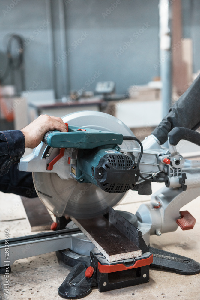 Fototapeta premium Furniture production or craft concept: worker sawing the wood surface of furniture part with saw machine