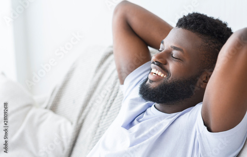 Pleased black man relaxing at home on couch
