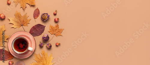 Autumn Flat lay composition. Cup of tea, autumn dry bright leaves, roses flowers, orange circle, cones, decorative pomegranate, cinnamon sticks on brown beige background top view. Autumn, fall concept photo