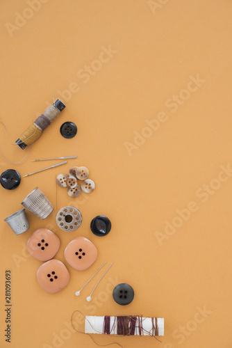 Thread spools; buttons; needle; thimble and button on an orange backdrop