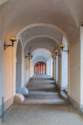 Arched house with in white color with lamps on the walls in Prague on the Hradcany square. Historic windows on the wall. Paving stones in the floor and grandstand on the walls © Marco