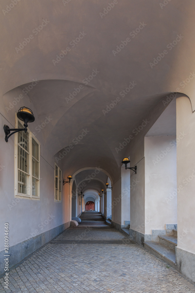 Gallery in the archway House with gray stones and lamps on the walls in Prague on the Hradcany square. Historic windows on the wall. Paving stones in the floor and grandstand on the walls