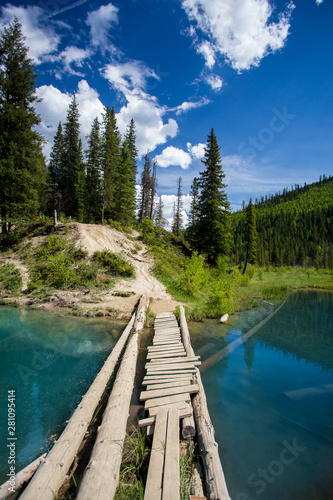 A rickety bridge crossing a bright blue lake in the Rockies photo