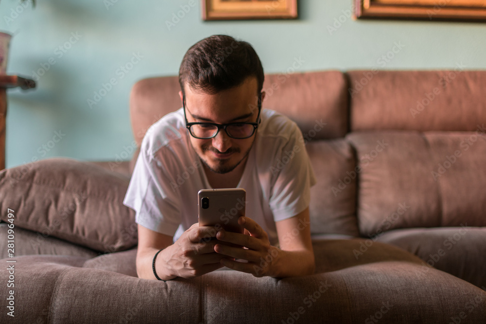 Man using mobile phone while lying on sofa at home Man using mobile phone while lying on sofa at home