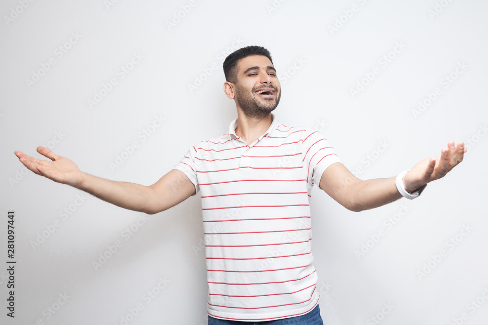 Portrait of happy handsome bearded young man in striped t-shirt standing with wide raised arms and looking at camera with toothy smile. indoor studio shot, isolated on white background. Portrait of happy handsome bearded young man in striped t-shirt standing with wide raised arms and looking at camera with toothy smile. indoor studio shot, isolated on white background.
