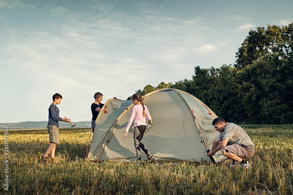 Family set up tent camp at sunset, beautiful summer landscape. Tourism, hiking and traveling in nature. - obrazy, fototapety, plakaty 
