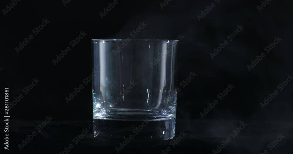 An empty whiskey, alcohol glass against a black background and floating smoke An empty whiskey, alcohol glass against a black background and floating smoke