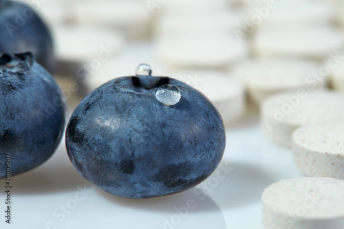 Three ripe blueberries on a background of tablets spread out on a light surface. Concept: natural vitamins. Close up.